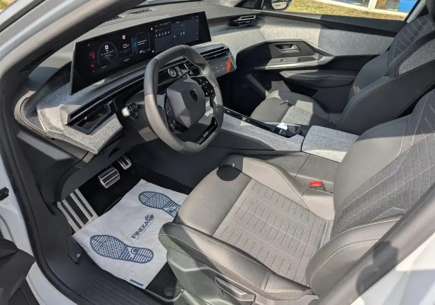 Vue intérieure côté conducteur du Peugeot 5008 blanc 2025, montrant le volant compact et l'écran panoramique incurvé.