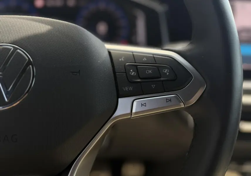 Gros plan sur le volant cuir noir du Volkswagen Taigo 2025, avec commandes multifonctions et logo VW central.