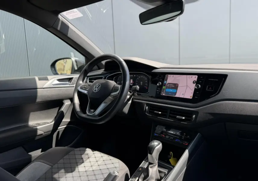 Vue intérieure côté conducteur du Volkswagen Taigo noir 2025, volant multifonctions et écran tactile avec navigation visible.