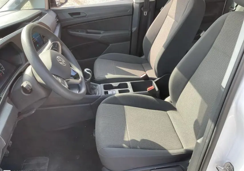 Vue intérieure côté conducteur du Volkswagen Caddy blanc Candy 2024 avec sièges tissu gris et volant multifonctions.