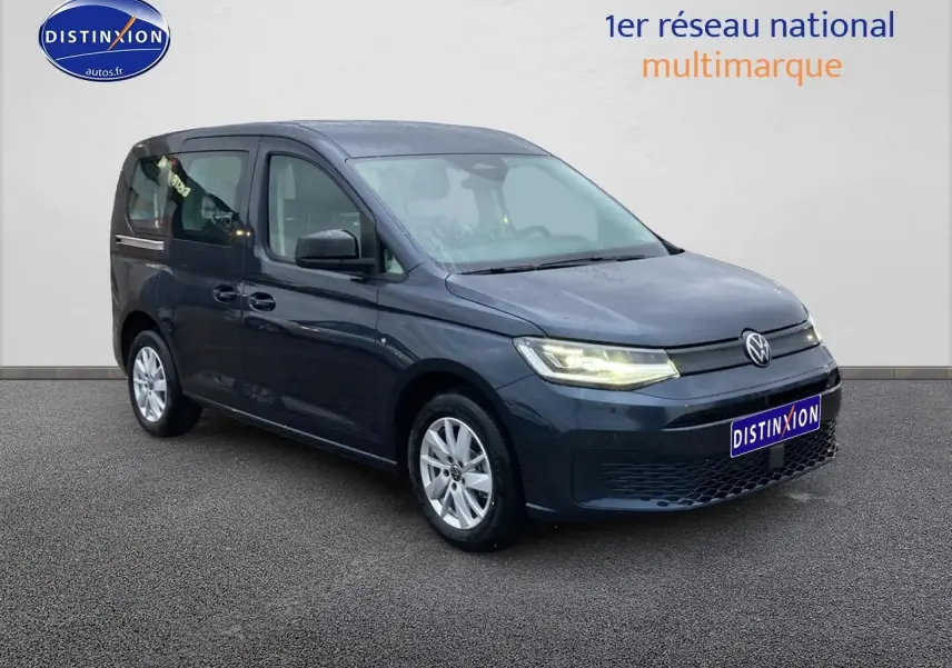 Volkswagen Caddy 2025 bleu métallisé en 3/4 avant droit avec phares allumés sur fond neutre.
