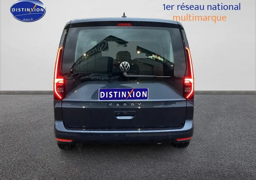 Vue arrière d'un Volkswagen Caddy bleu métallisé 2025 avec feux allumés et logo visible sur fond neutre.
