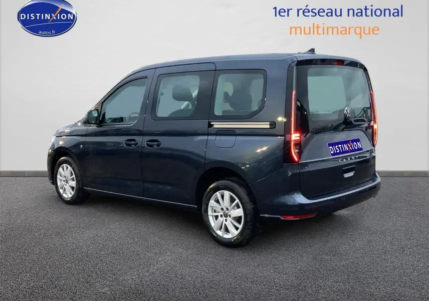 Vue 3/4 arrière droite d'un Volkswagen Caddy bleu métallisé avec feux arrière allumés sur fond neutre.