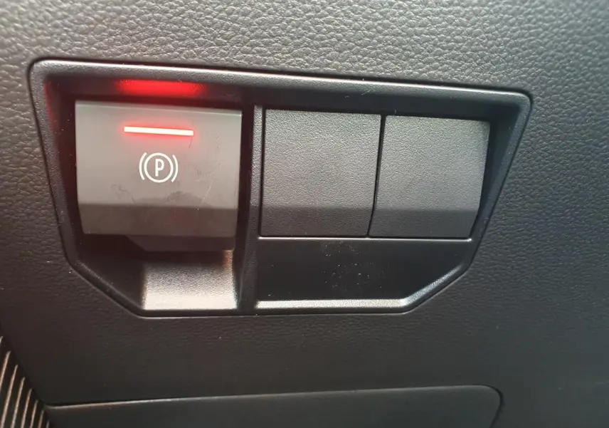 Gros plan sur le bouton de frein de stationnement électrique allumé dans l'habitacle noir du Dacia Dokker Van gris schiste.