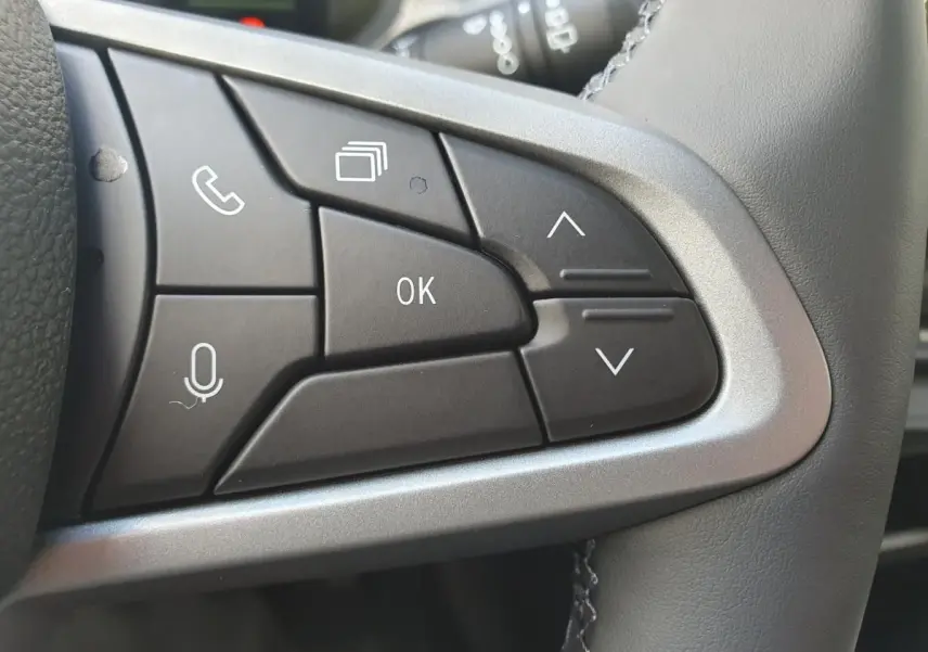 Gros plan sur les commandes multifonctions noires du volant du Dacia Dokker Van gris schiste, avec boutons de navigation et appel.