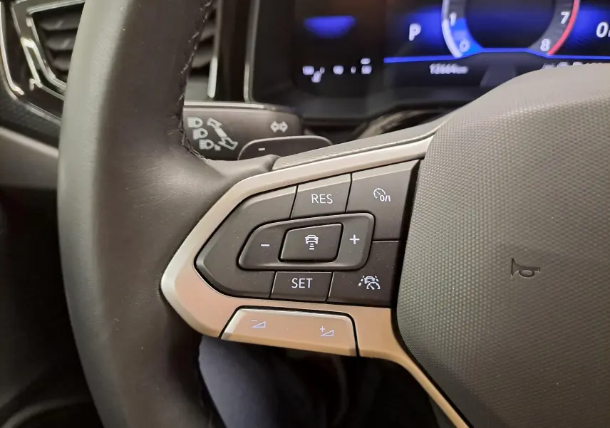Gros plan sur les commandes au volant à gauche du Volkswagen Taigo 2025, avec finition argentée et affichage numérique en arrière-plan.