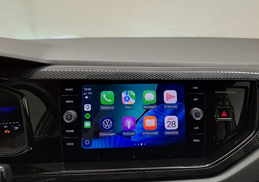 Écran tactile central du Volkswagen Taigo 2025, affichant interface connectée avec commandes autour, finition noire texturée.