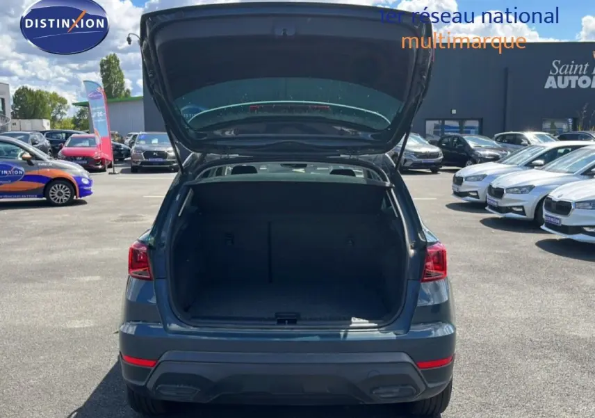 Vue arrière d'un SEAT Arona bleu Fjord avec coffre ouvert, toit blanc visible, sur un parking extérieur.