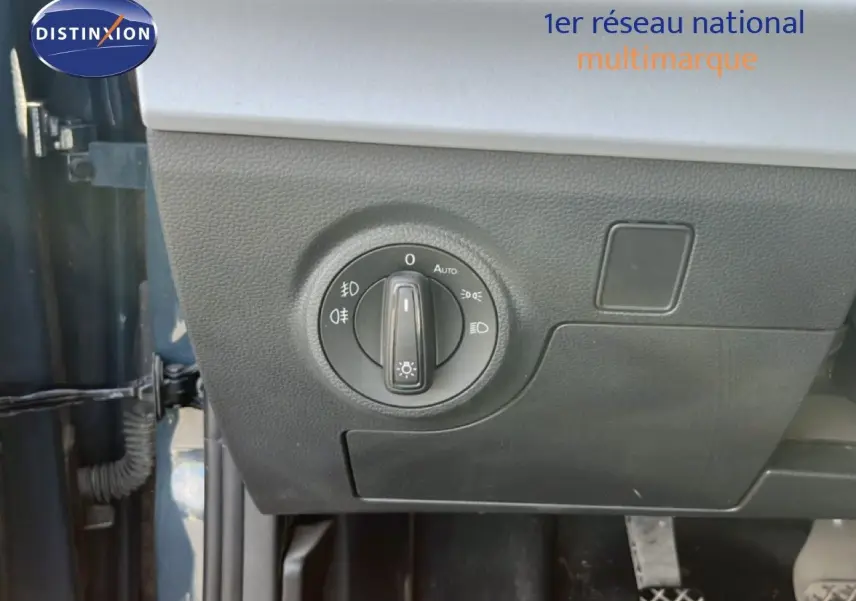 Gros plan sur la commande des phares à gauche du tableau de bord d’un SEAT Arona bleu Fjord avec toit blanc.
