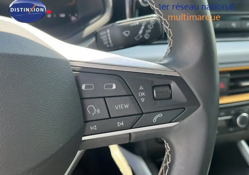 Gros plan sur le volant multifonction noir avec surpiqûres blanches du SEAT Arona 2025, intérieur gris et console visible.