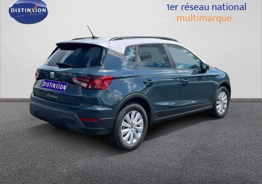 Vue 3/4 arrière droite d'une SEAT Arona bleu Fjord avec toit blanc, stationnée sur sol gris devant un mur clair.