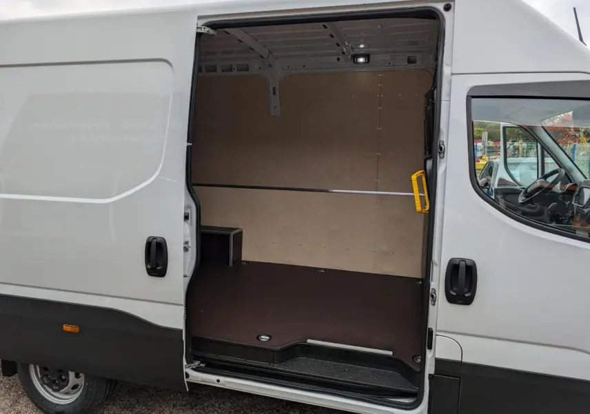 Vue latérale droite d’un Iveco Daily blanc 2025 avec porte coulissante ouverte montrant l’intérieur aménagé du compartiment de chargement.