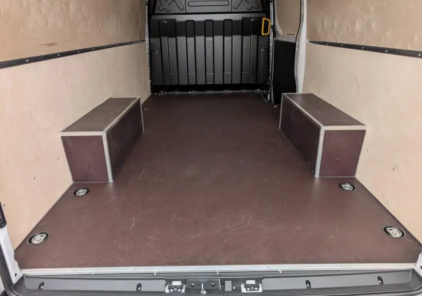 Vue intérieure arrière du fourgon Iveco Daily blanc avec plancher antidérapant marron et habillages latéraux en bois clair.