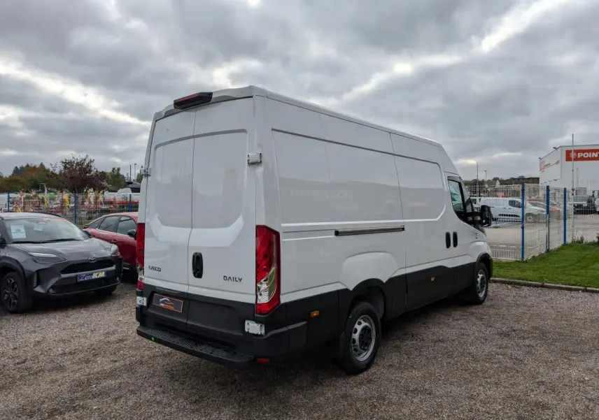 IVECO Daily blanc vu 3/4 arrière droit, portes arrière fermées et calandre noire visible sur parking.
