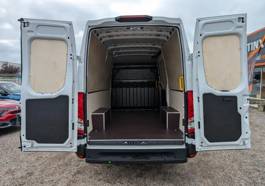 Vue arrière d’un utilitaire Iveco Daily blanc 2025 avec portes ouvertes et intérieur de chargement protégé par habillages bois et plancher antidérapant.