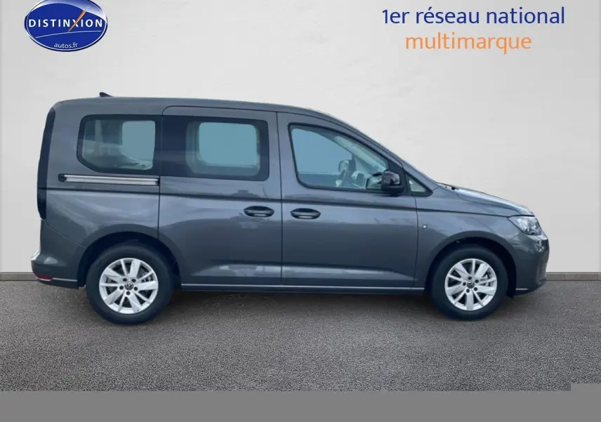 Profil droit d'un Volkswagen Caddy gris indien 2025 avec barres de toit et jantes alliage visibles.