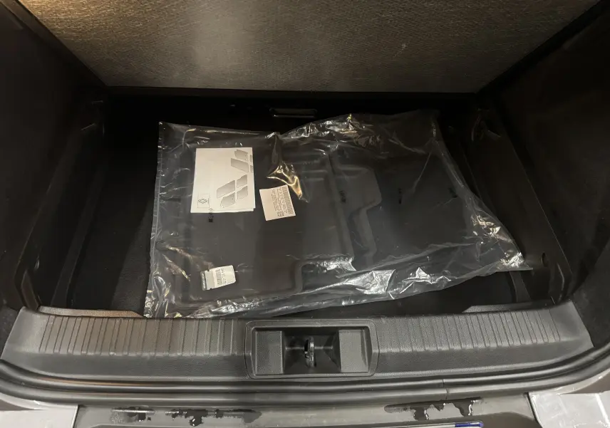 Coffre ouvert d’un Renault Captur gris foncé, vue plongeante montrant des tapis neufs emballés à l’intérieur.