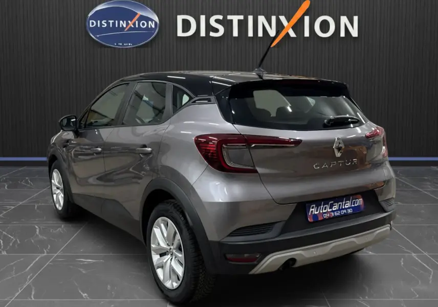 Vue 3/4 arrière droite d'un Renault Captur gris foncé avec toit noir, en intérieur devant un mur noir marqué Distinxion.
