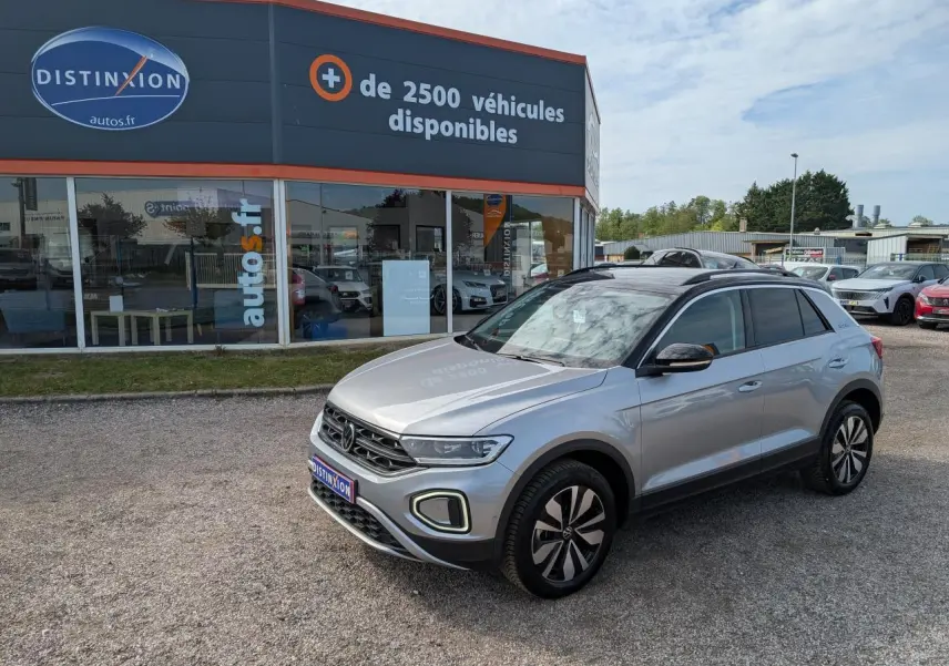 Volkswagen T-Roc gris 3/4 avant droit avec toit noir et jantes alliage 17 pouces, stationné devant un showroom.