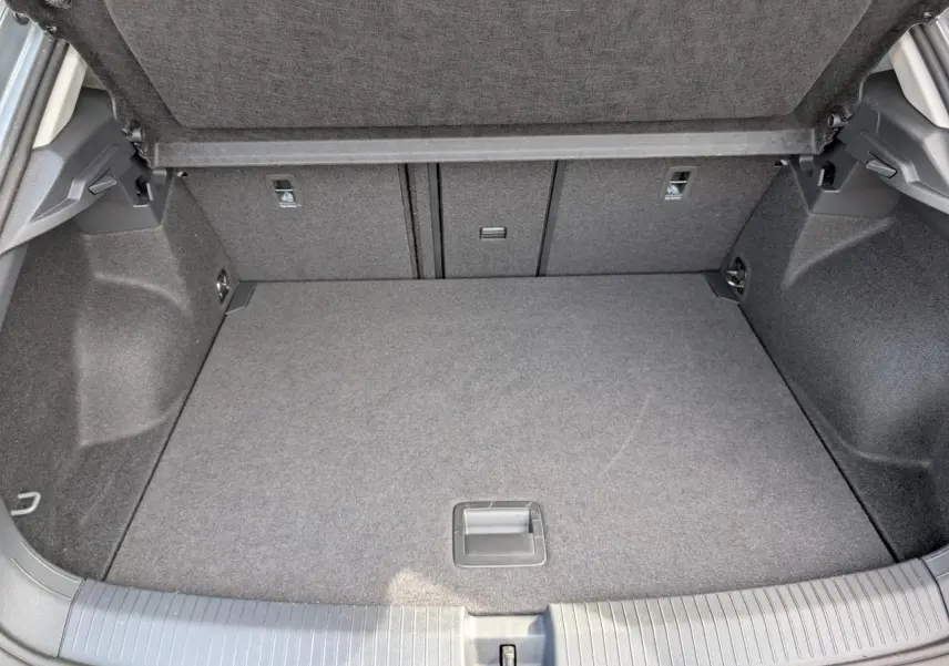 Coffre ouvert vu de l'arrière d'un Volkswagen T-Roc gris, avec plancher plat et revêtement tissu gris.