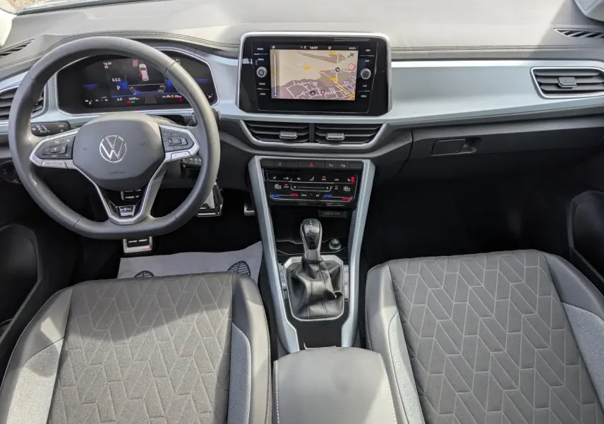 Vue intérieure avant du Volkswagen T-Roc 2025 gris, avec tableau de bord digital et écran tactile central.