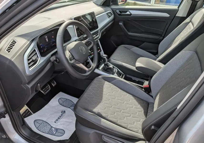 Intérieur avant droit du Volkswagen T-Roc gris 2025 avec sièges tissu gris et tableau de bord digital.