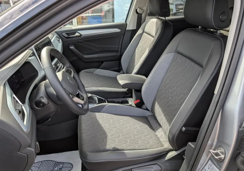 Vue intérieure côté conducteur du Volkswagen T-Roc gris 2025, mettant en valeur les sièges avant en tissu et cuir bicolore.