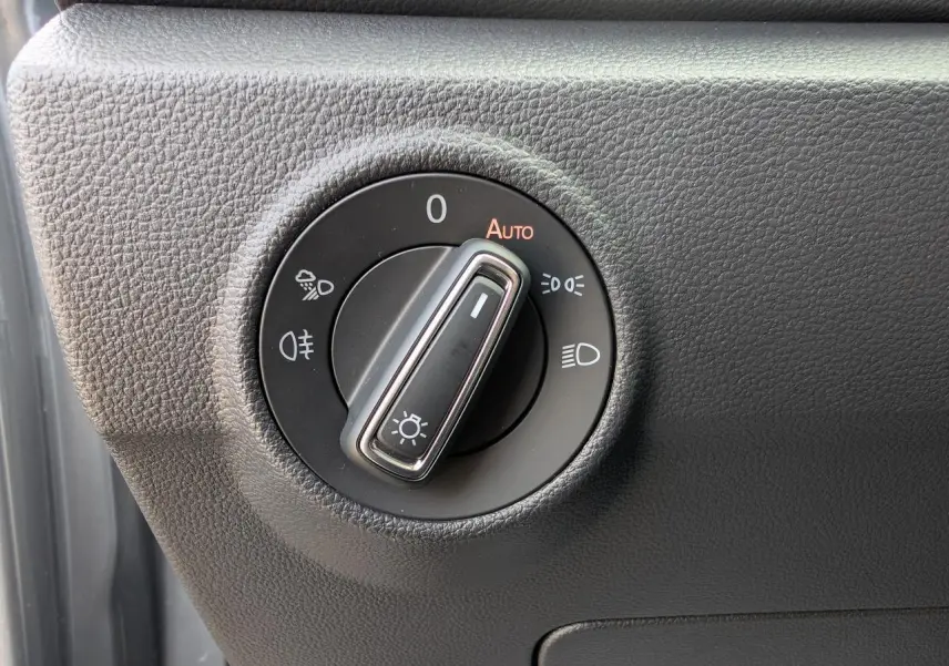 Gros plan sur le bouton de commande des phares du Volkswagen T-Roc gris, situé côté gauche du tableau de bord.