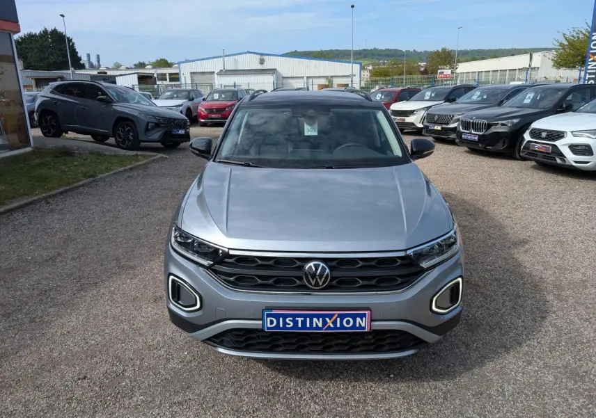 Volkswagen T-Roc gris métallisé vue de face, avec calandre noire et feux LED distinctifs allumés.