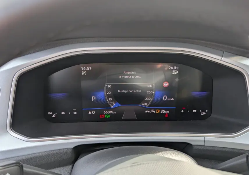 Vue rapprochée du tableau de bord digital du Volkswagen T-Roc gris, affichant la vitesse et alertes moteur.