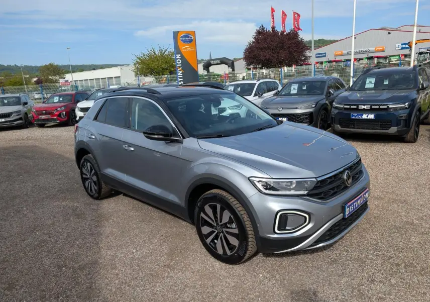 Volkswagen T-Roc gris métallisé en 3/4 avant droit avec jantes alliage et toit noir sur parking extérieur.