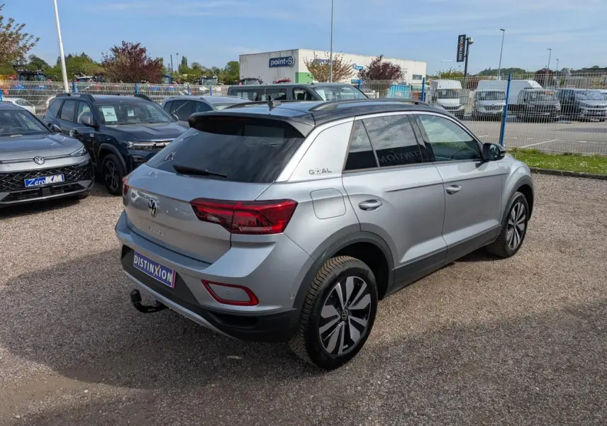 Vue 3/4 arrière droite d'un Volkswagen T-Roc gris métallisé avec toit noir et attelage amovible visible.