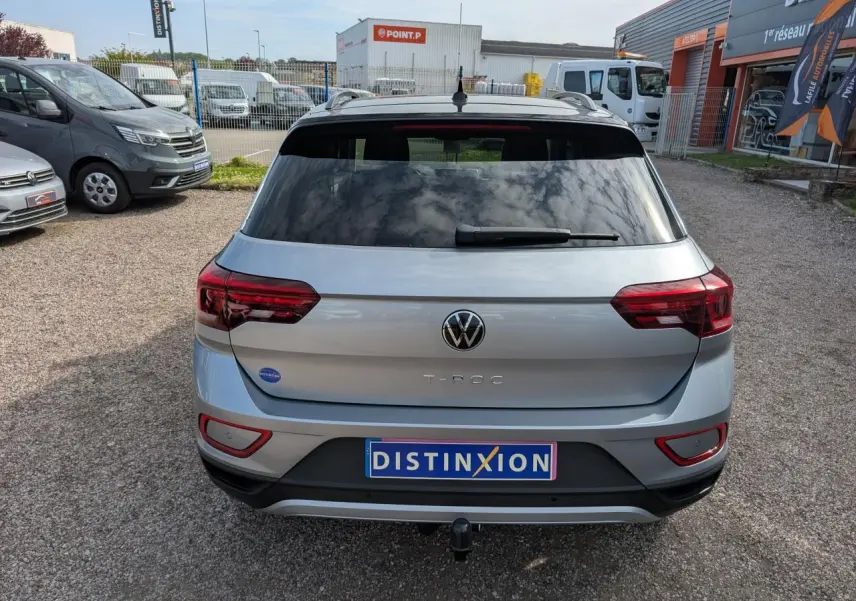 Vue arrière d'un Volkswagen T-Roc gris avec attelage amovible et vitres arrière teintées, stationné en extérieur.
