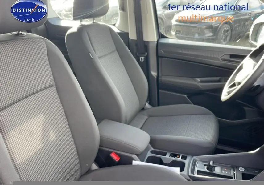 Vue intérieure côté droit du Volkswagen Caddy 2025, sièges tissu gris double grid avec accoudoirs centraux réglables.