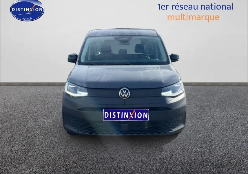Vue frontale d'un Volkswagen Caddy gris pur 2025 avec phares allumés et calandre épurée.