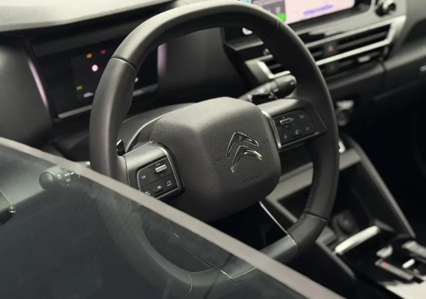 Vue rapprochée du volant en cuir noir de la Citroën C4 2024 avec commandes intégrées et tableau de bord numérique.