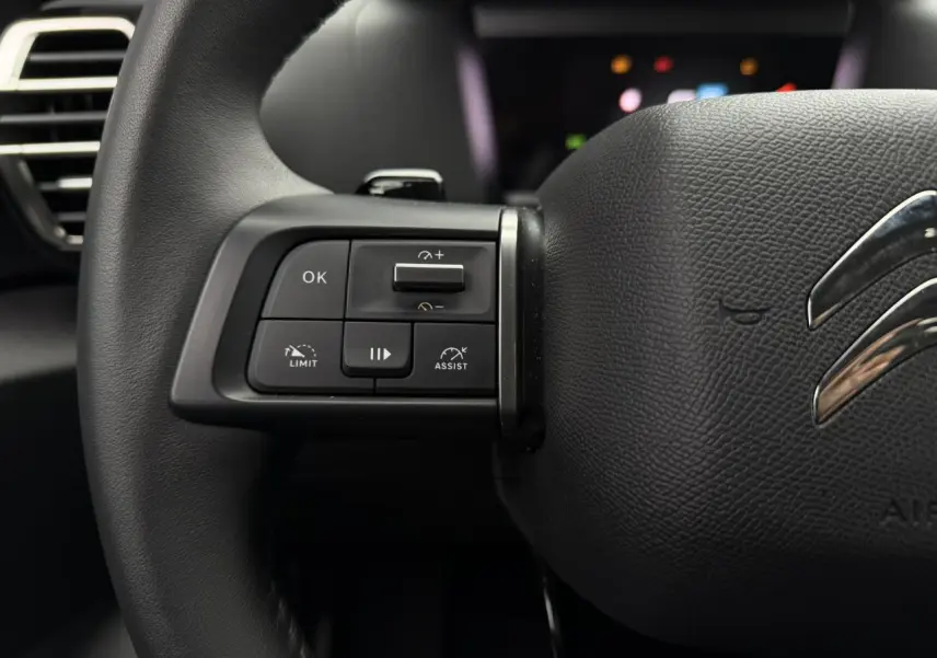 Gros plan sur les commandes gauche du volant noir en cuir du Citroën C4 2024, avec logo chromé visible.