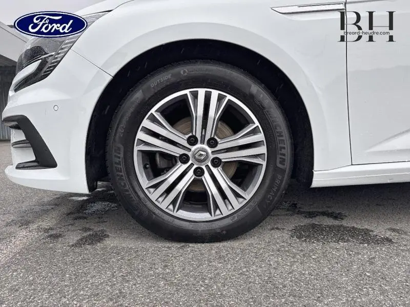 Gros plan sur la roue avant gauche de la Renault Mégane blanche avec jante alliage et logo Renault central.
