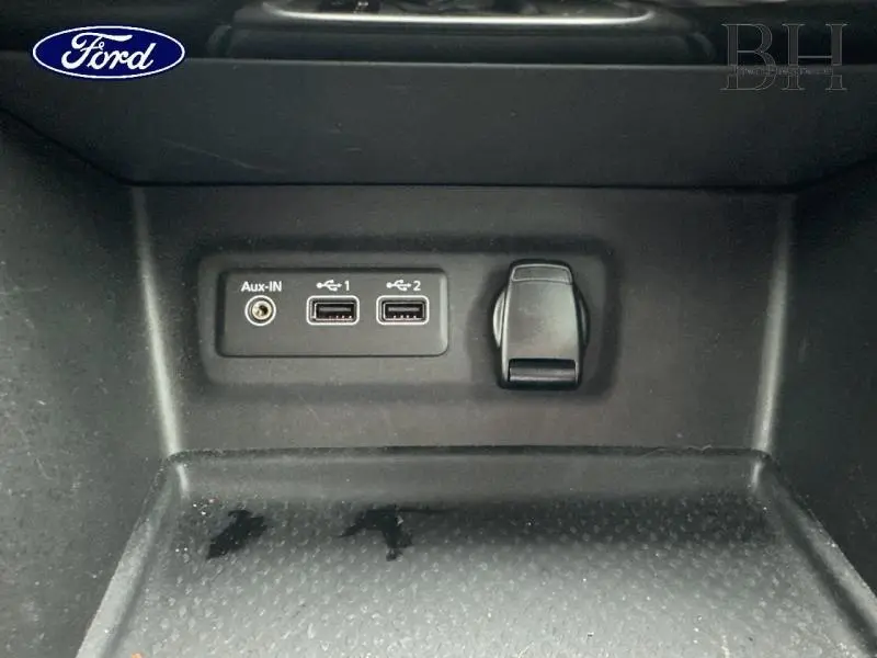 Gros plan sur la console centrale noire avec prises USB, entrée Aux et prise 12V dans une Renault Mégane blanche.