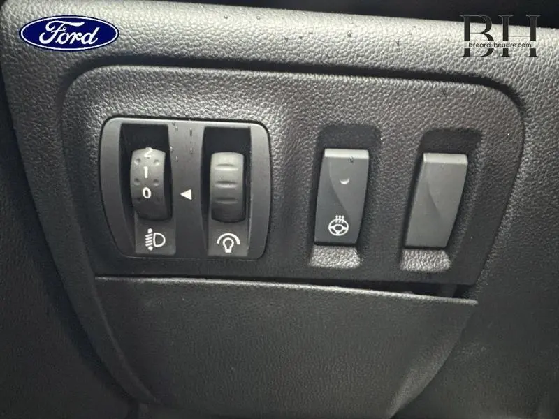 Gros plan sur les commandes noires du tableau de bord d'une Renault Mégane blanche, boutons d'éclairage et chauffage volant visibles.