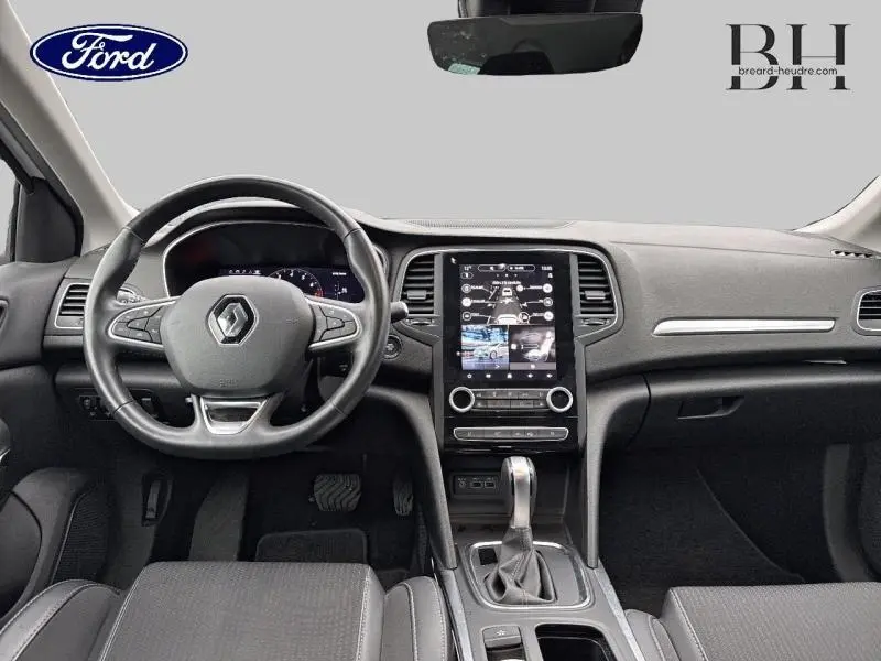 Vue intérieure avant du tableau de bord et volant noir de la Renault Mégane blanche, avec écran tactile vertical et levier de boîte auto.