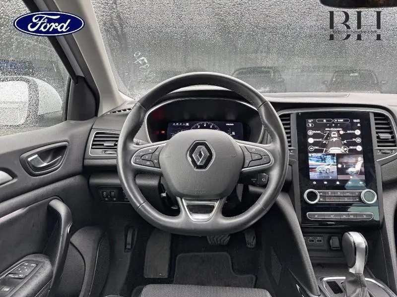 Vue intérieure centrée sur le volant noir de la Renault Mégane blanc, avec tableau de bord numérique et écran tactile vertical.