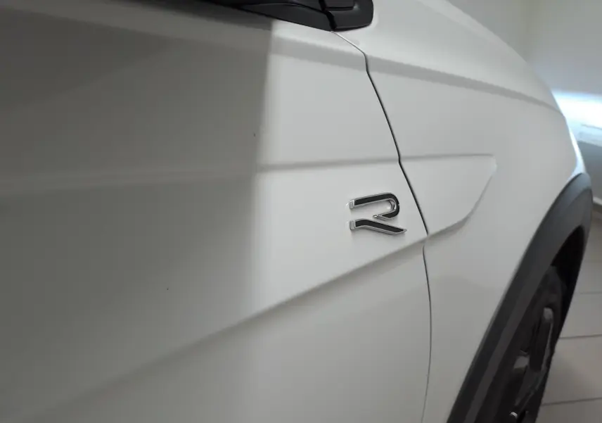 Gros plan sur l'aile avant droite blanche du Volkswagen Taigo avec logo R-Line brillant et jante noire partielle visible.