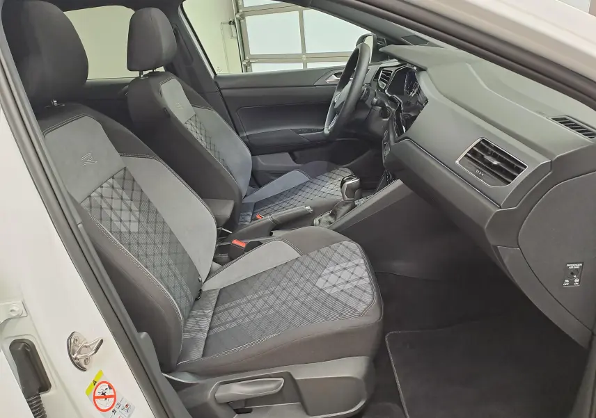 Vue intérieure côté gauche du Volkswagen Taigo 2025 avec sièges sport gris à motifs et tableau de bord noir.