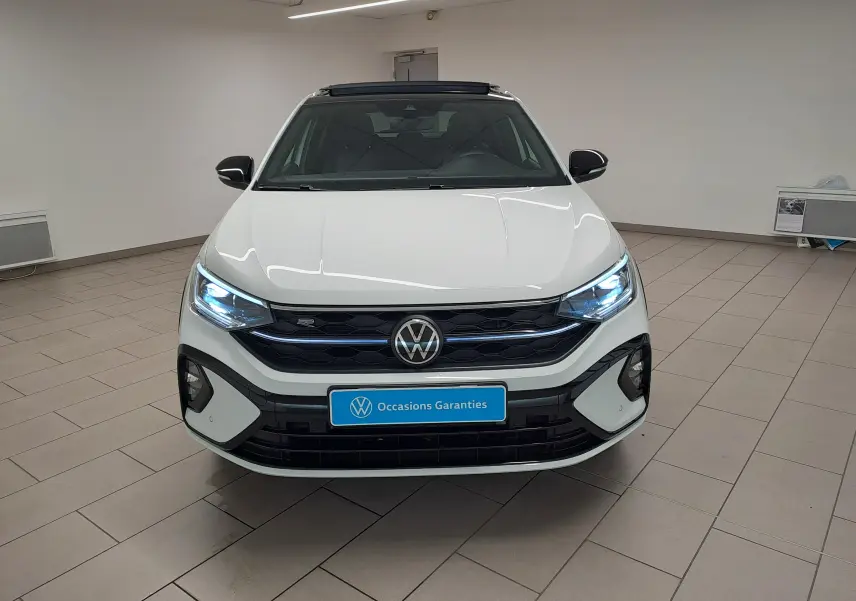Vue frontale d'un Volkswagen Taigo blanc pur avec toit noir, calandre R-Line et phares LED allumés en intérieur showroom.