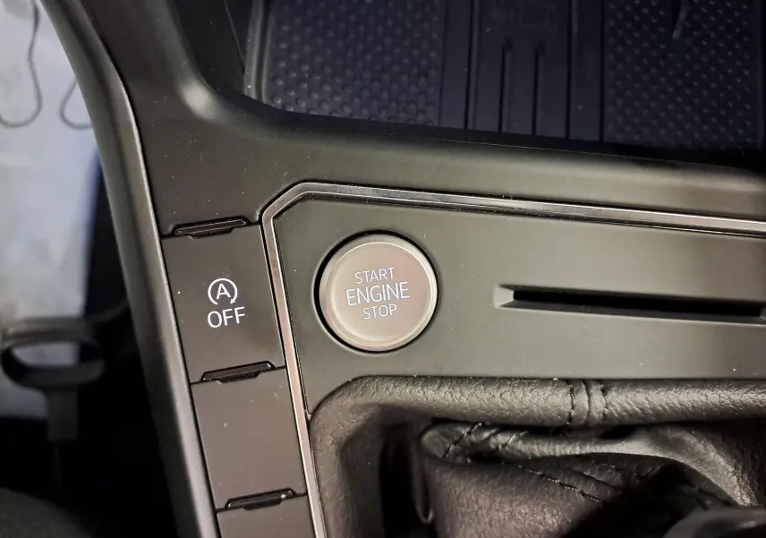 Gros plan sur le bouton Start Engine Stop et la commande Auto Stop/Start désactivée dans la console centrale noire du Volkswagen Taigo.