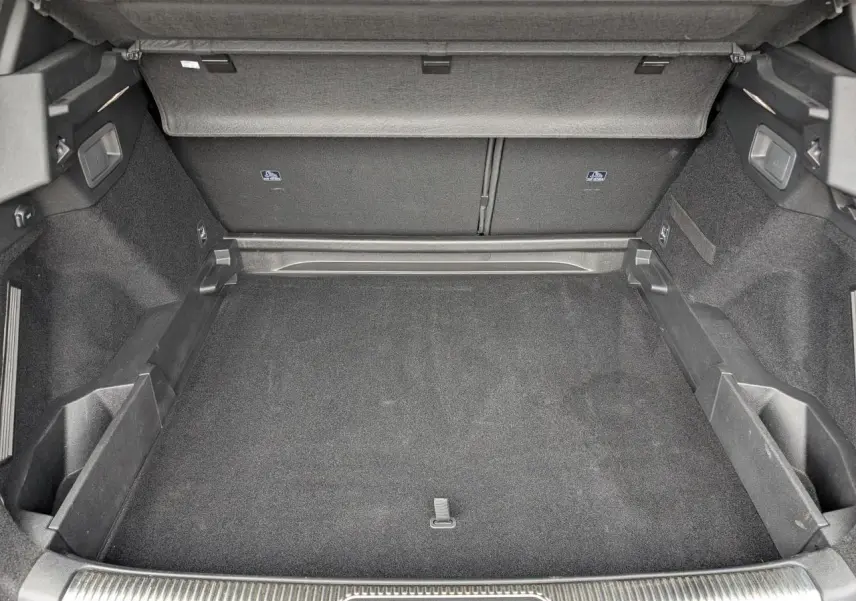 Coffre ouvert vu de face, intérieur noir avec tapis et rangements latéraux, sans chargement visible.