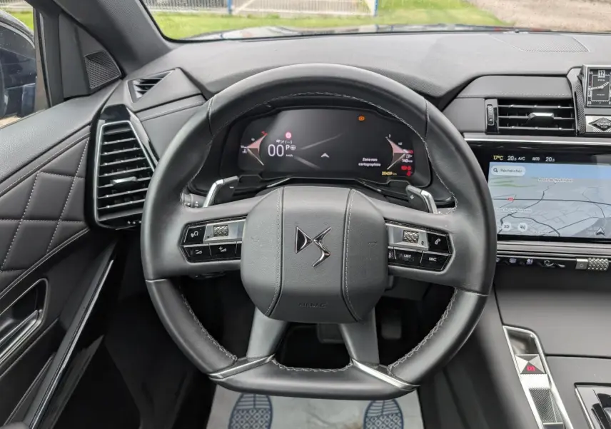 Vue intérieure centrée sur le volant cuir noir du DS7 2024 avec tableau de bord numérique et écran tactile latéral.