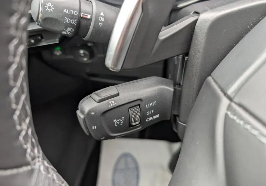 Gros plan sur la commande de régulateur de vitesse noir dans l’habitacle du DS7 2024, côté gauche du volant.