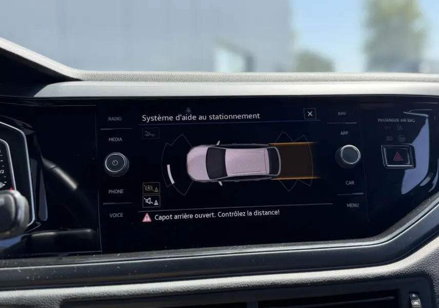 Écran central du Volkswagen Taigo TSI 116 R-Line affichant l'aide au stationnement avec alerte capot arrière ouvert.